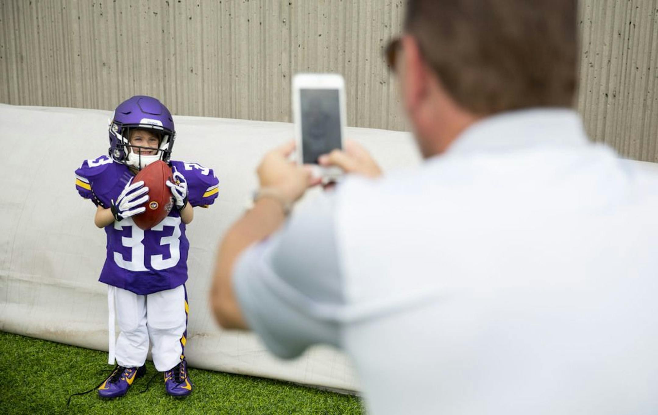 (From left) Elliana Kojoen posed in an oversized Dalvin Cook jersey and football gear while her dad, Mike, snapped a picture. ALEX KORMANN • alex.kormann@startribune.com The Minnesota Vikings opened up their first full day of training camp on Friday July 26, 2019 at TCO Performance Center in Eagan, MN. Doors opened to fans at 11AM to watch their favorite players practice and get excited for the 2019 NFL season.