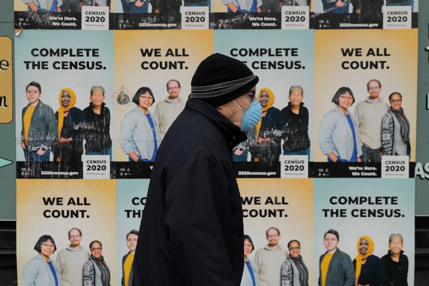 A man wearing a mask walks past posters encouraging participation in the 2020 Census, Wednesday, April 1, 2020, in Seattle's Capitol Hill neighborhood.