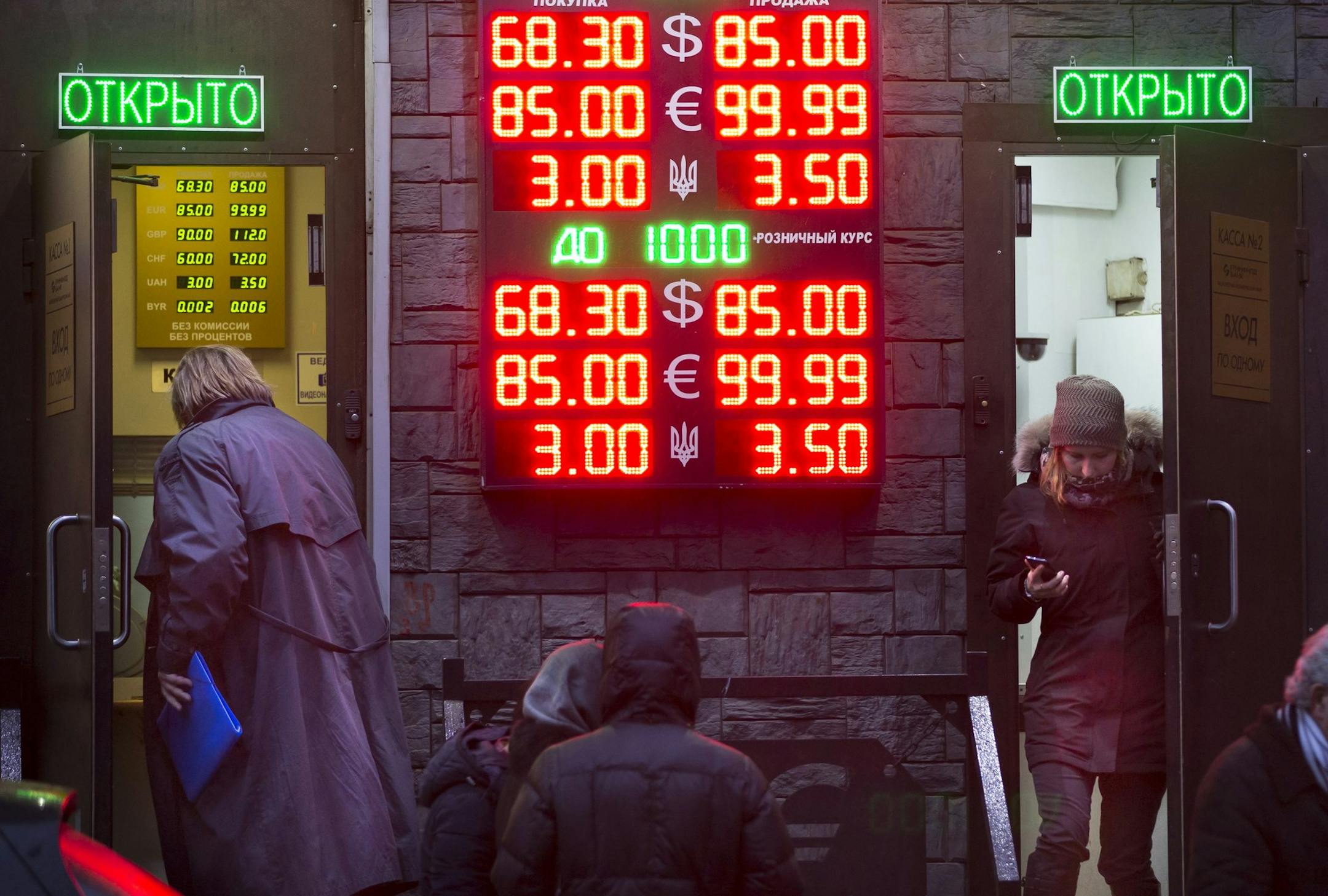 People wait to exchange their currency as signs advertise the exchange rates at a currency exchange office in Moscow, Russia, Tuesday, Dec. 16, 2014. The Russian ruble came under intense selling pressure Tuesday, falling at one point by a catastrophic 20 percent to a new historic low despite a massive pre-dawn interest rate hike from Russia's Central Bank. Russian officials were clearly rattled even though state television urged citizens not to panic.The top two figures indicate the spread on th