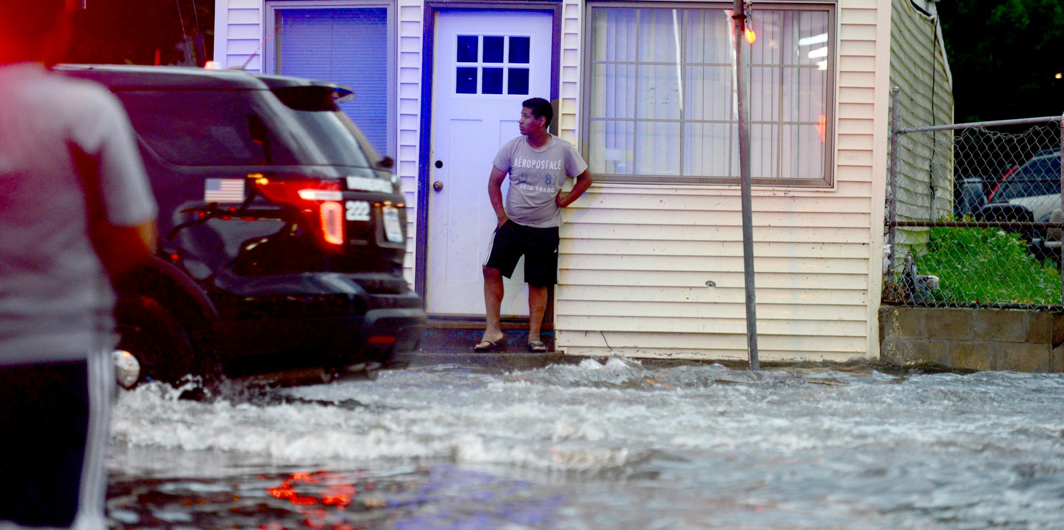 A car drove through the flooded street near the intersection of Lowry and Monroe Aves in Minneapolis as pedestrians watched.