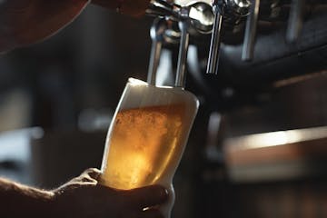 Fresh beer filling the glass directly from the tap. With extra foam spilling over glass.