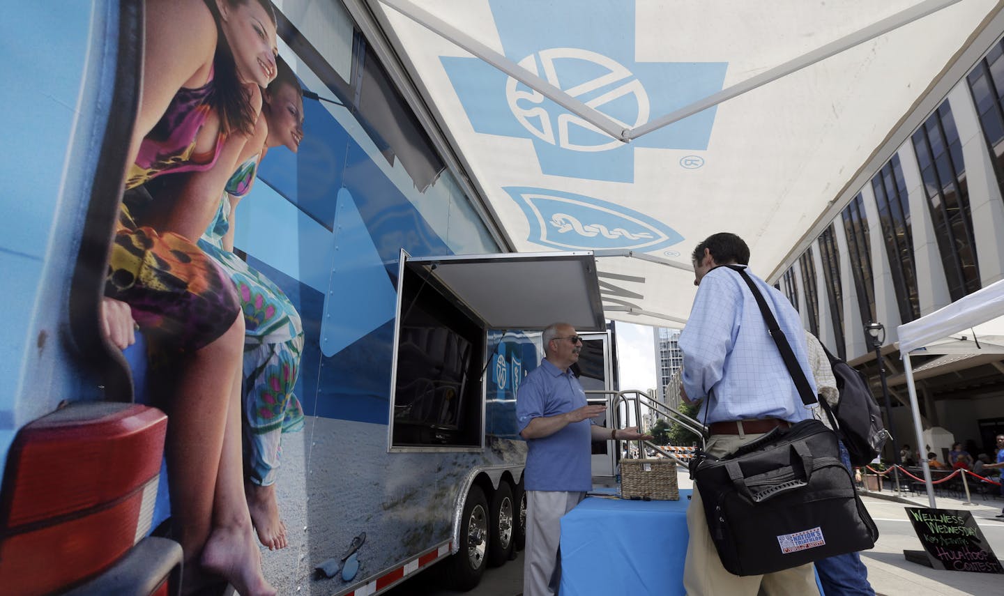 FILE - In this photo taken Wednesday, July 17, 2013, Blue Cross Blue Shield of North Carolina employee Lew Borman, left, helps a customer outside a trailer at the downtown farmer's market in Raleigh, N.C. Dozens of health insurers say higher-than-expected care costs and other expenses blindsided them this year, and they&#xed;re going to have to hike individual insurance prices well-beyond 10 percent for 2016. (AP Photo/Gerry Broome, File)