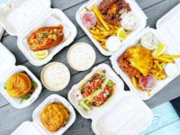 A picnic table with many dishes from Coastal Seafoods' cafe in Minneapolis: burgers, tacos, soft-shell crab and lobster rolls.
