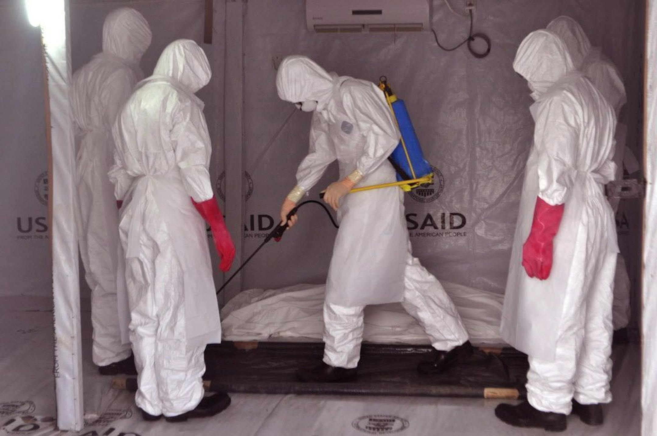 In this photo taken on Friday, Nov. 28, 2014, health workers wearing Ebola protective gear spray the shrouded body of a man with disinfectant as they suspect he died from the Ebola virus, at a USAID, American aid Ebola treatment center at Tubmanburg on the outskirts of Monrovia, Liberia. Two months ago, the World Health Organization launched an ambitious plan to stop the deadly Ebola outbreak in West Africa, by isolating 70 percent of Ebola sick by December 1, 2014, but on Sunday Nov. 30, 2014,