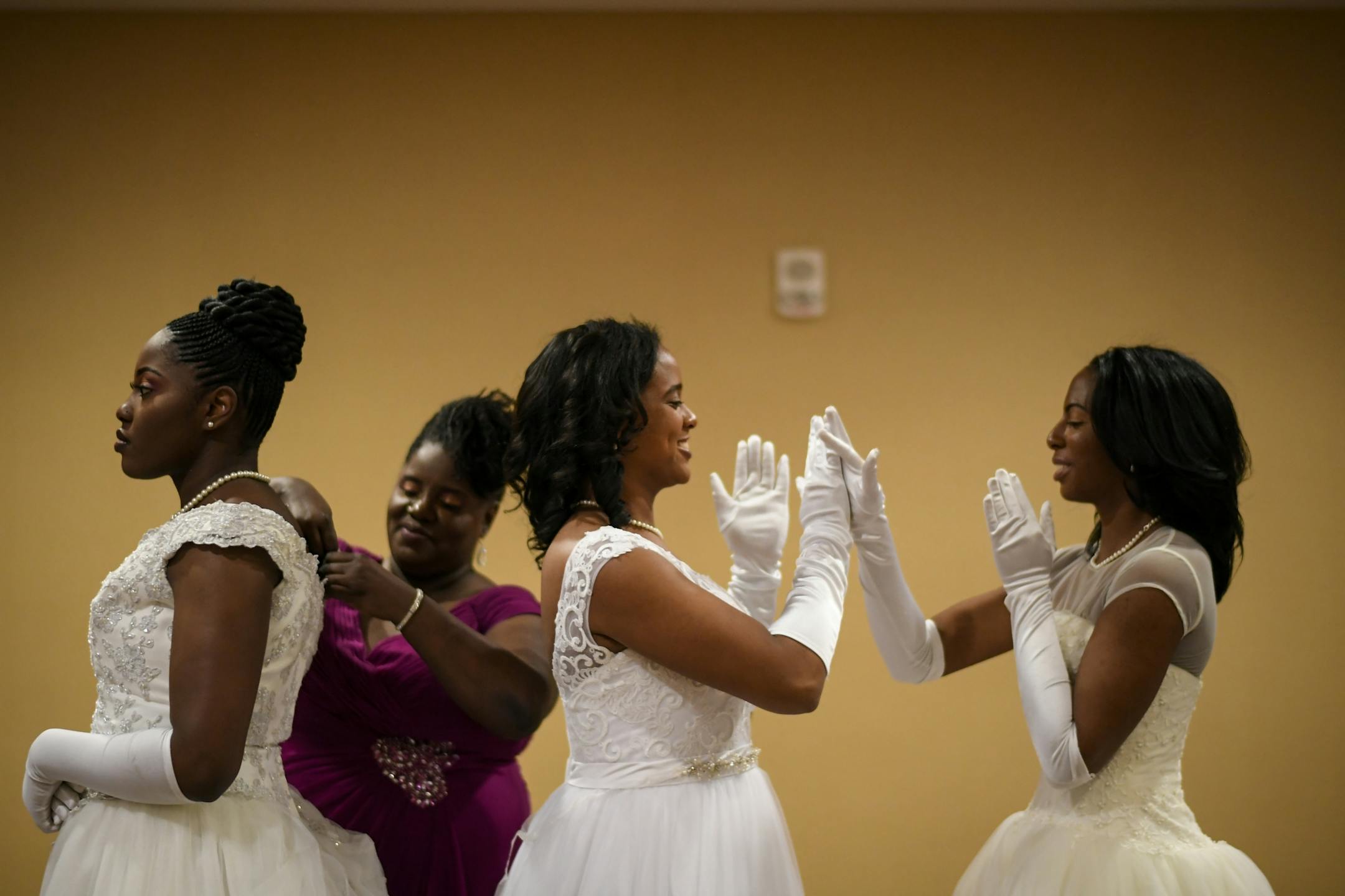 From left, debutante Ayo Olagbaju stood in line as her mother, Shana Moses, fixed her dress. To their right, Morgan Phillips and Alyssa Story played a hand-clapping game Saturday night before their introductions at the cotillion ball.