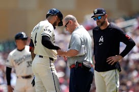 The Twins' Carlos Correa is looked at by a team trainer after he was hit by a pitch during the first inning against the Houston Astros on Sunday.