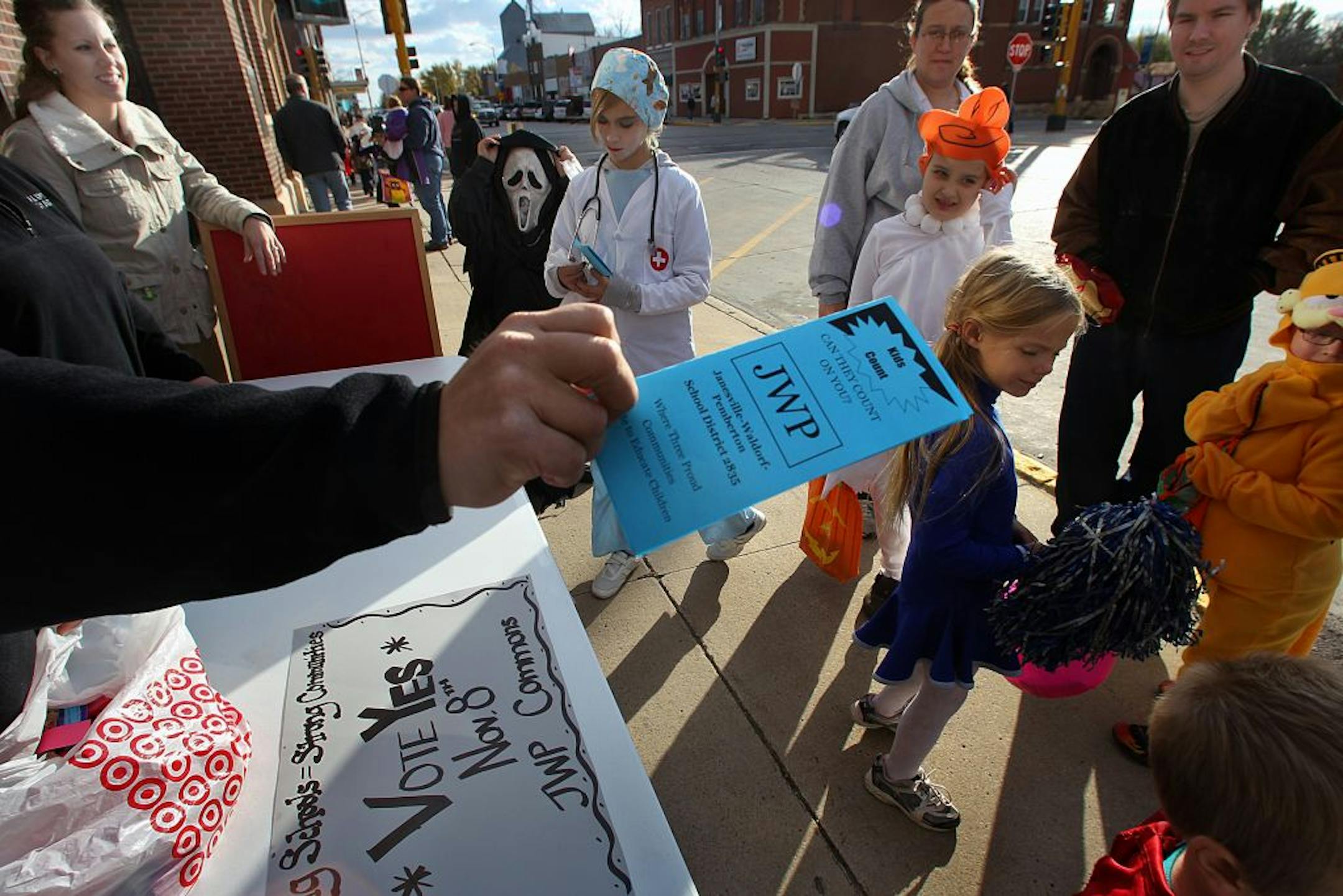 Volunteers handed out literature about the upcoming school referendum and Halloween candy in downtown Janesville during a trick-or-treat event held by local businesses. The hand with brochure is that of Janesville-Waldorf-Pemberton Elementary School second grade teacher Jeremy Erler (who is also the elementary dean of students). At upper left is third grade teacher Claudia Roesler.