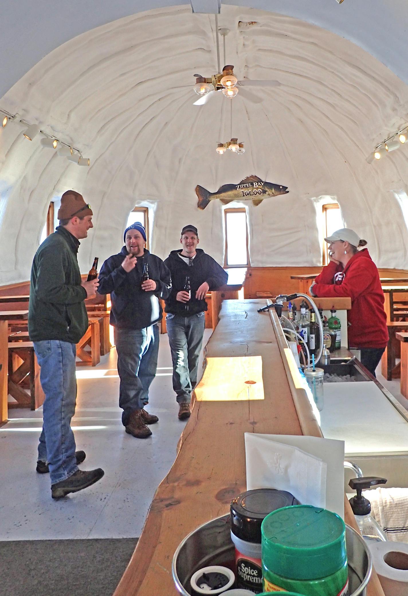 Three first-time visitors to the Igloo Bar tell fish stories to bartender Jenny Johnson. Below each wood bench along the walls are ice fishing holes that customers can rent for $5 an hour. This year, the bar is too close to a sandbar to fish, but it's open 6 days a week as a social outlet for anglers and snowmobilers on Zippel Bay. From left, the visitors from Missouri are Chris Woodring, Brandon Hensley and Lawrence Bryant.