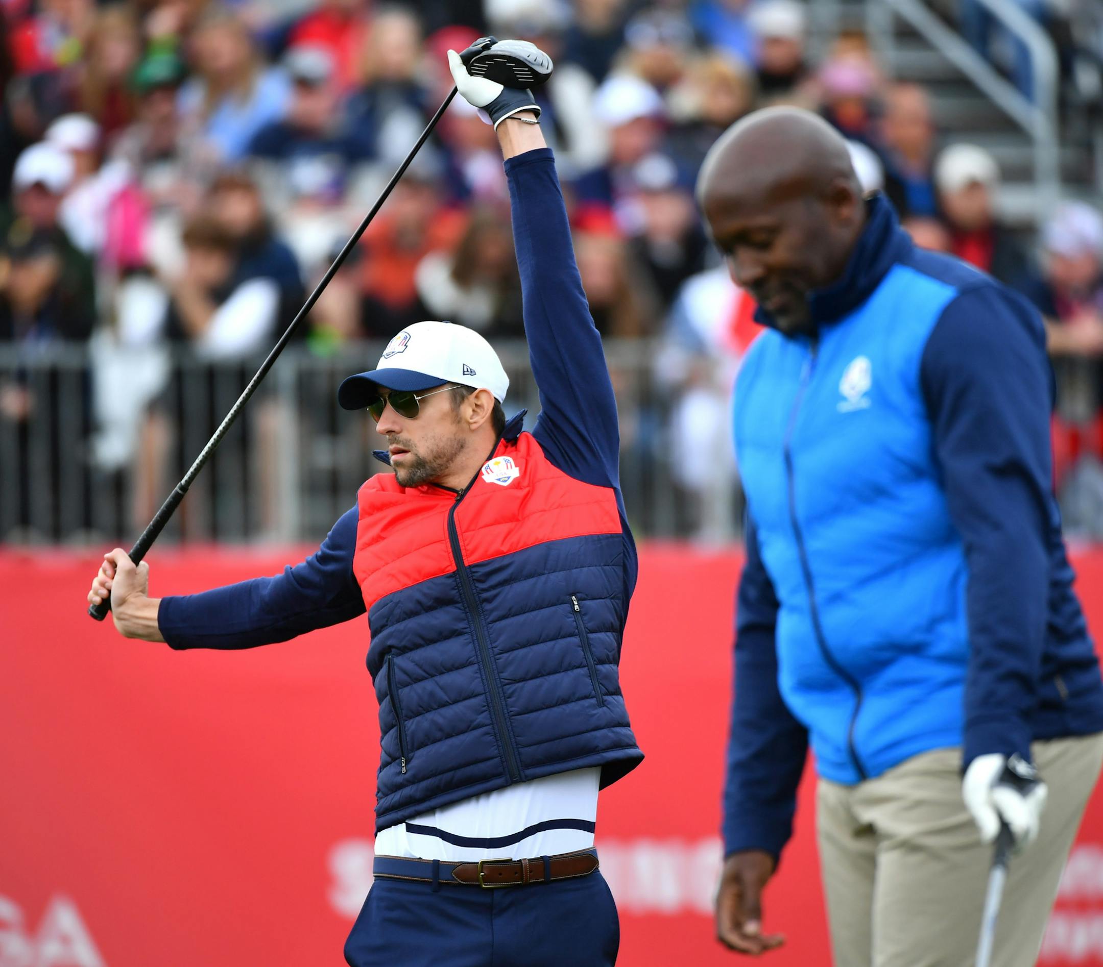 23 time Olympic gold medalist Michael Phelps stretched as retired English Olympic sprinter John Regis set up his shot at the first tee during the Ryder Cup Celebrity Match Tuesday. ] (AARON LAVINSKY/STAR TRIBUNE) aaron.lavinsky@startribune.com Team USA and Team Europe practiced for the Ryder Cup at Hazeltine National Golf Club on Tuesday, Sept. 27, 2016 in Chaska, Minn.