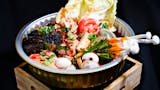 A hot pot filled with mushrooms, vegetables and sauce.