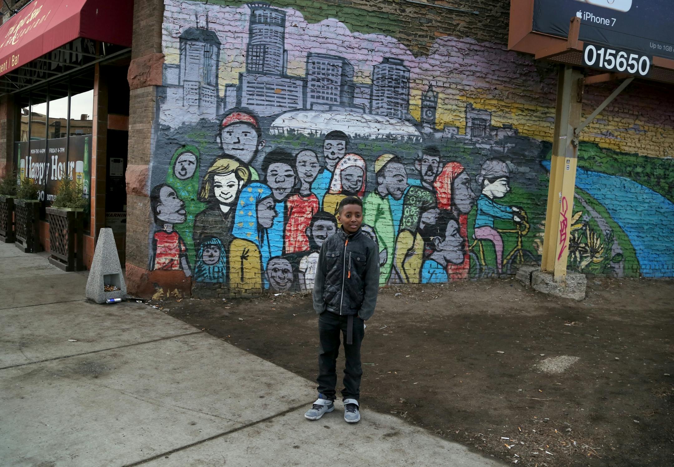 A young boy standing by a mural in the Cedar-Riverside are comes out to check out The Caravan of Love: A Walk of Love for Immigrants and Refugees.