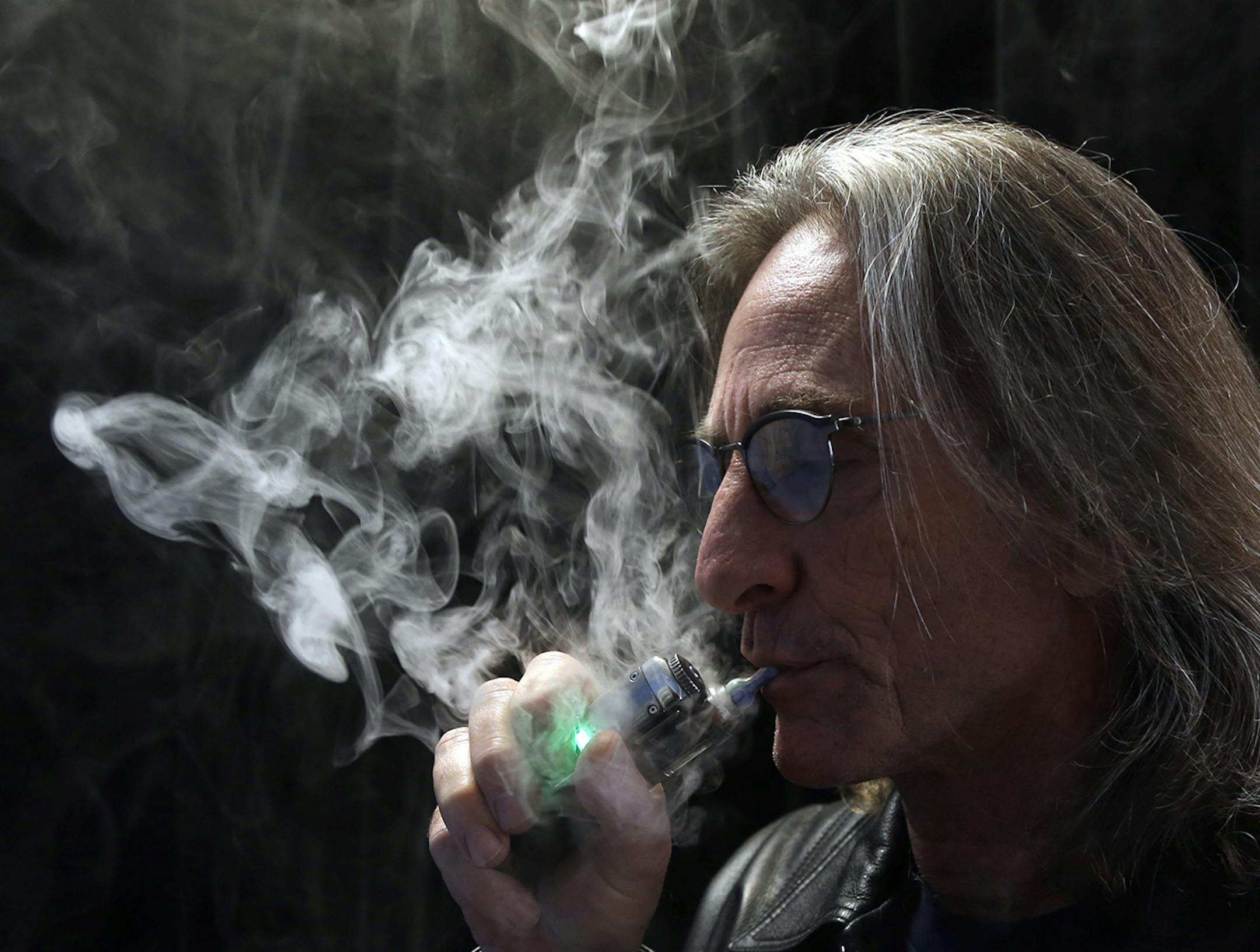 John Hartigan, proprietor of Vapeology LA, a store selling electronic cigarettes and related items, takes a puff of an electronic cigarette at his store in Los Angeles on Wednesday, Dec. 4, 2013. Two California cities have voted to ban electronic cigarettes in public places, and Los Angeles on Wednesday moved to prohibit their sale to minors. (AP Photo/Reed Saxon) ORG XMIT: MIN2013121014155645