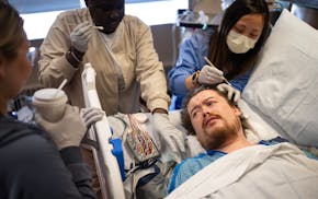 ICU patient Spencer Kallestad is prepped for an EEG by EEG technicians Maria Thao, from right, and Nyaware Puoch, as registered nurse Claire Anderson