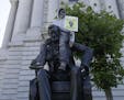 A person holds a sign while sitting on a statue of Abraham Lincoln outside of City Hall in San Francisco, Saturday, June 13, 2020, at a protest over t