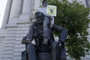 A person holds a sign while sitting on a statue of Abraham Lincoln outside of City Hall in San Francisco, Saturday, June 13, 2020, at a protest over t