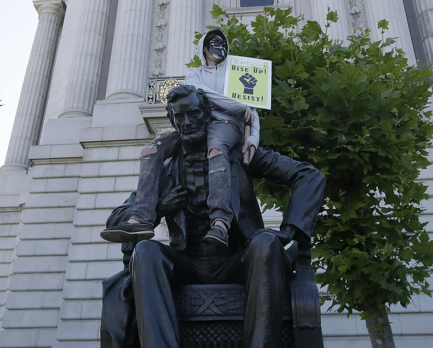 A person holds a sign while sitting on a statue of Abraham Lincoln outside of City Hall in San Francisco, Saturday, June 13, 2020, at a protest over the May 25th death of George Floyd who died after being restrained by Minneapolis police officers. (AP Photo/Jeff Chiu)