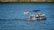 A pontoon boat headed downriver, along the Mississippi River, past Levee Park in Winona, Minnesota.
