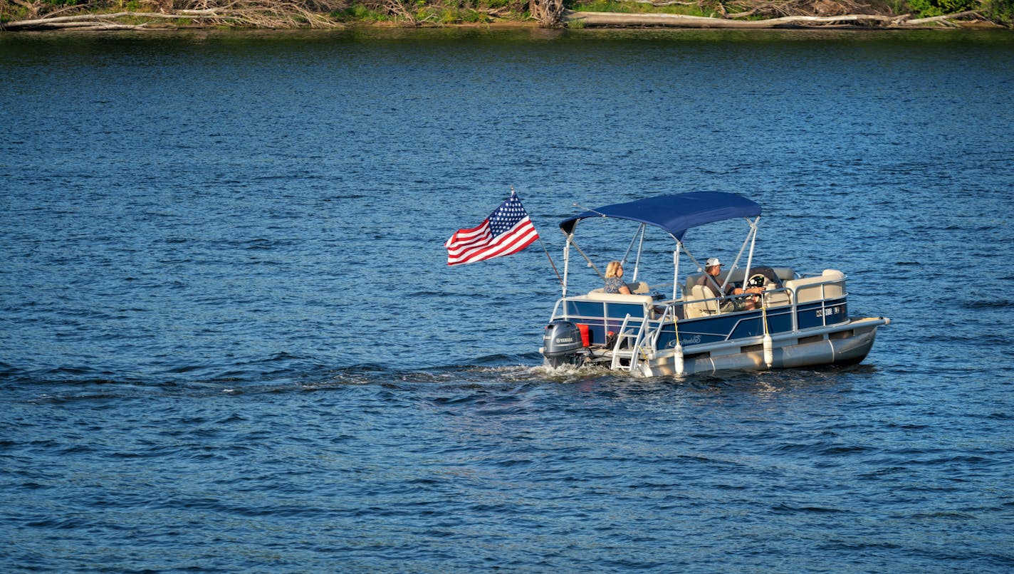 A pontoon boat headed downriver, along the Mississippi River, past Levee Park in Winona, Minnesota.