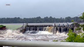 This image taken from video provided by WGBA-TV, shows water breaching a section of a dam, left, along the Little Wolf River, Friday, July 5, 2024, in