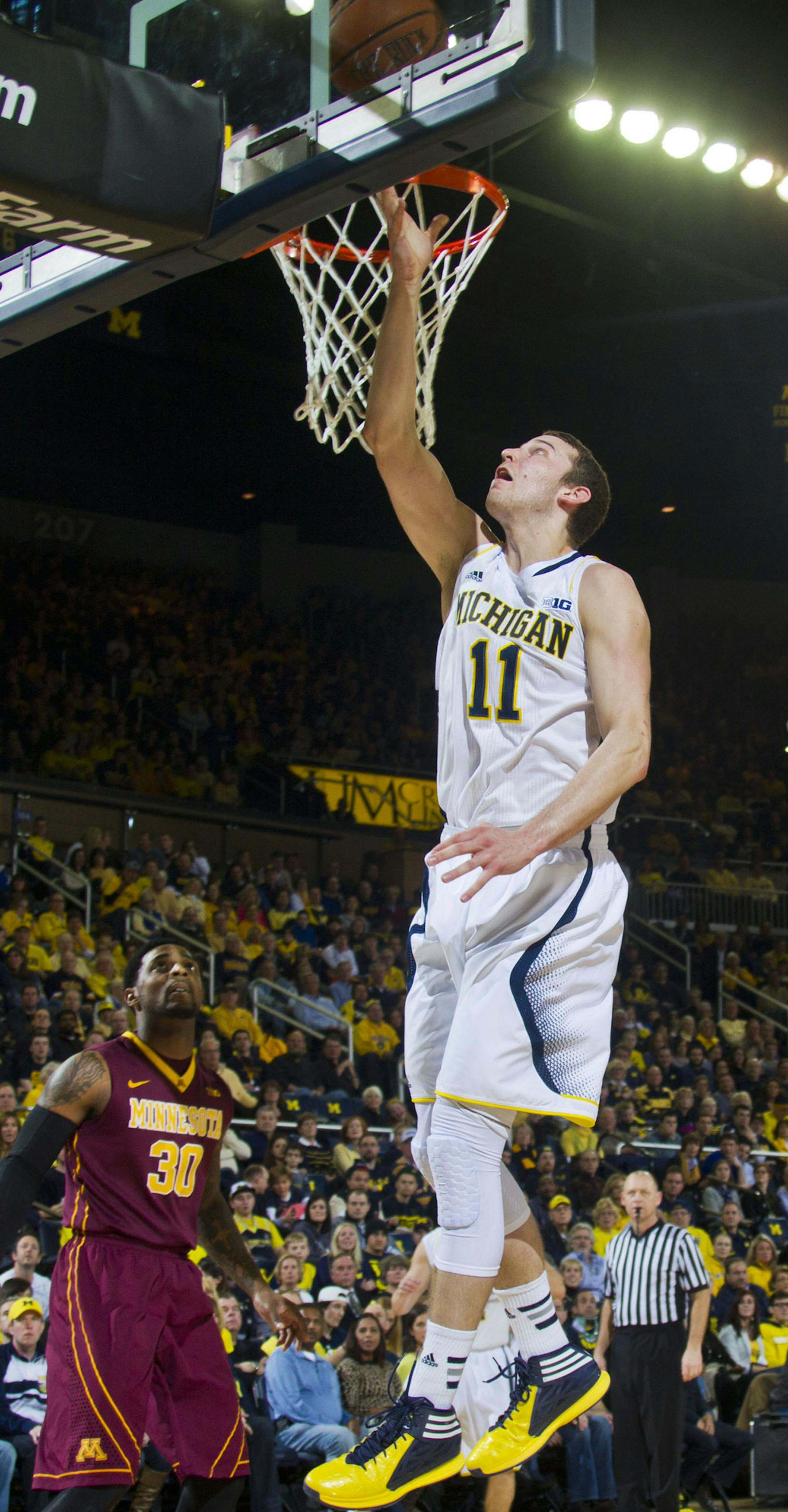 Michigan guard Nik Stauskas (11) makes a layup while defended by Minnesota guard Daquein McNeil (5) during the first half of an NCAA college basketball game in Ann Arbor, Mich., Saturday, March 1, 2014. (AP Photo/Tony Ding)