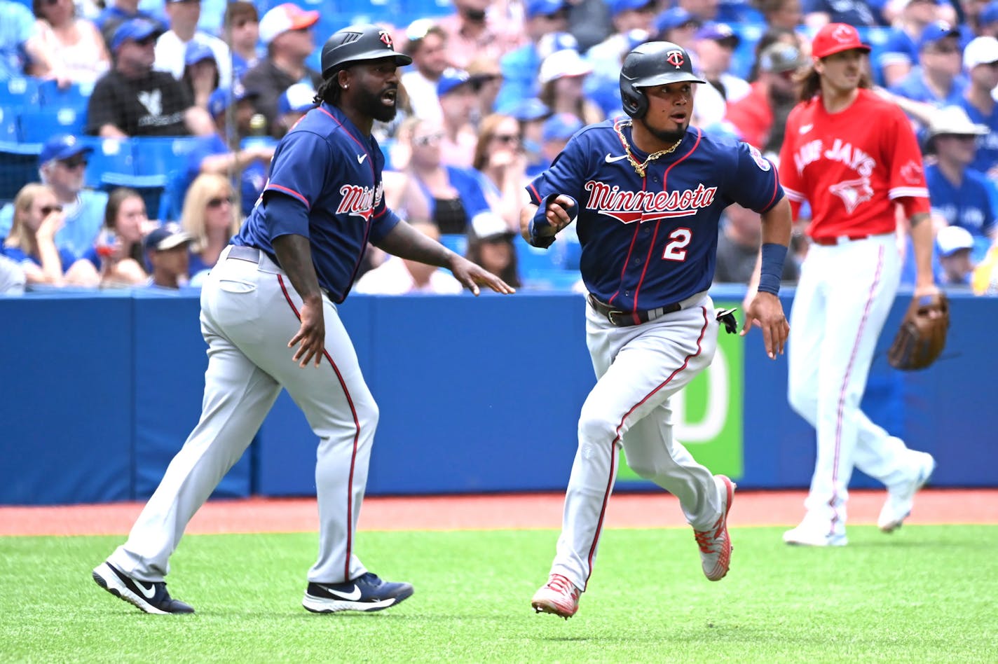 Minnesota Twins third base coach Tommy Watkins, left, instructs designated hitter Luis Arraez (2) to run home after Jorge Polanco reached base safely on fielding error by Toronto Blue Jays' Teoscar Hernandez (not shown) in the first inning of a baseball game in Toronto, Sunday, June 5, 2022. (Jon Blacker/The Canadian Press via AP)