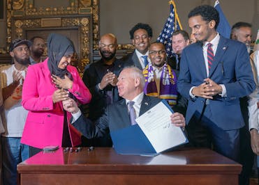 Minnesota Governor Tim Walz gave a pen to Rep. Hodan Hassan, DFL-Minneapolis, (left in pink) after a ceremonial signing event for the pay minimums for