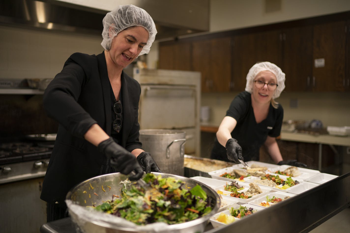 Chowgirls Killer Catering president Maari Cedar James tossed a salad while executive chef Elizabeth Mullen doled out portions of mushroom chicken as they assembled meals in the kitchen of Hope Presbyterian Church in Richfield.