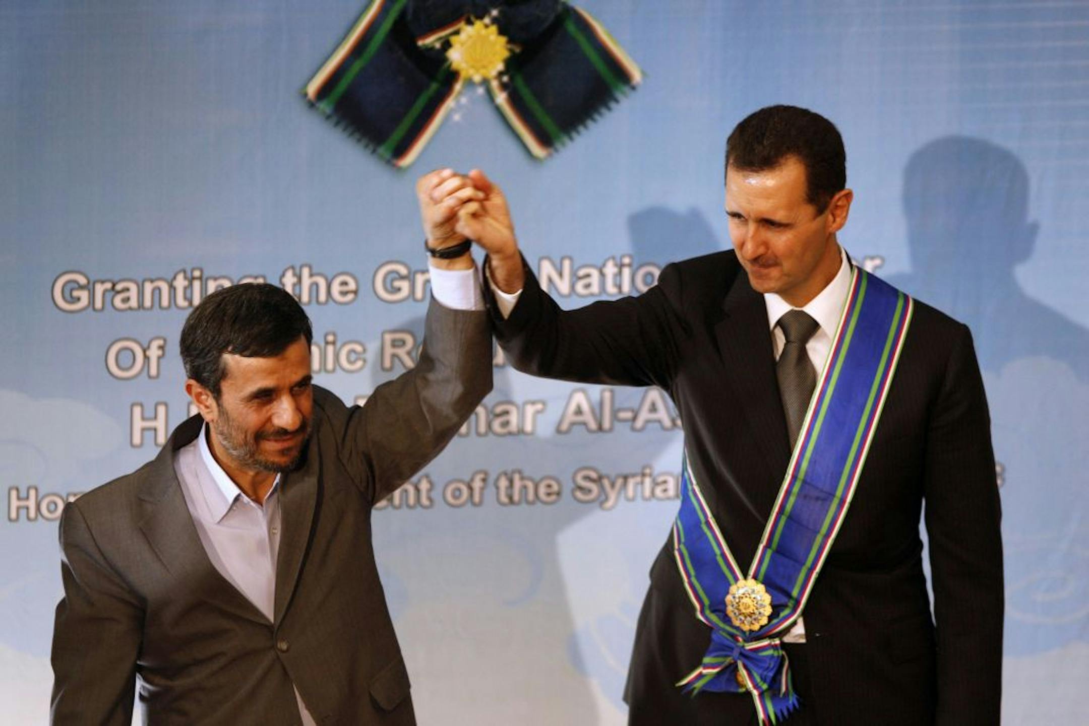 2010 photo: Iranian President Mahmoud Ahmadinejad, left, holds up the hand of his Syrian counterpart Bashar Assad after he awarded Iran's highest national medal to Assad, in a ceremony in Tehran, Iran.
