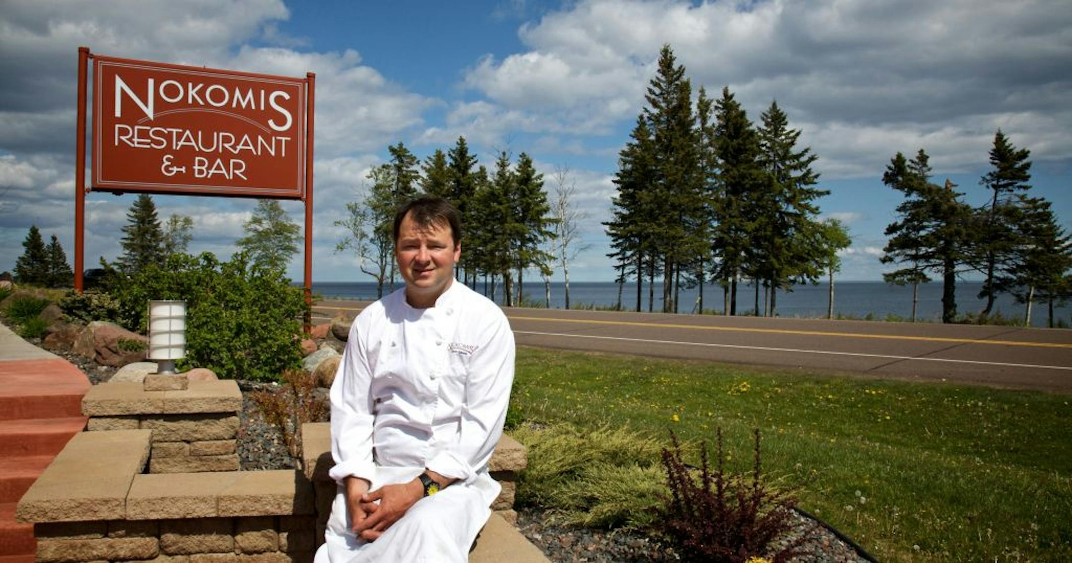 Chef Sean Lewis sits on wall in front of the Nokomis Restaurant & Bar that fronts Lake Superior.