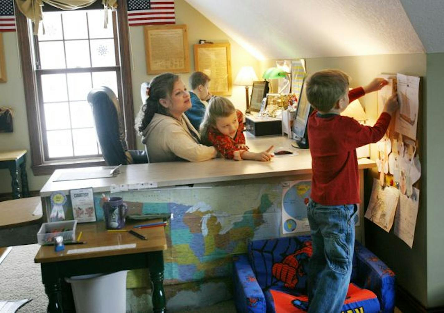 Jack Colombo, 6, hangs a coloring of a Viking ship from online history studies on the family bulletin board while mom Tami and sister Grace, 8, look on and older brother Jake, 13, works on an online physical science assignment.