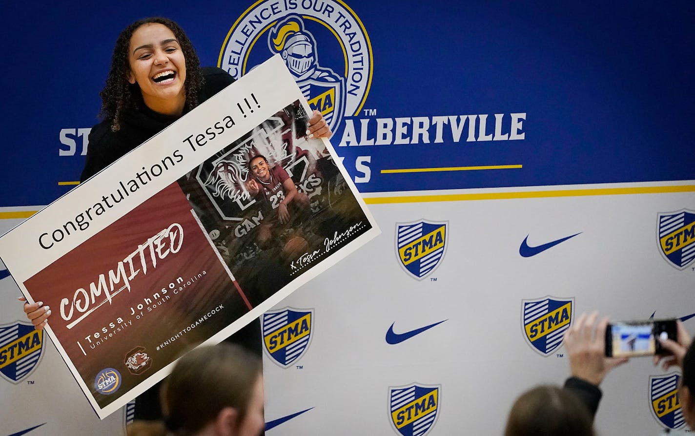 St. Michael-Albertville High basketball star Tessa Johnson, Minnesota's top-ranked girls basketball recruit, holds up a sign as she poses for photos after announcing that she would be attending the University of South Carolina on a basketball scholarship Wednesday, Oct. 19, 2022 during an event in the St. Michael-Albertville High gym in St. Michael, Minn. ]