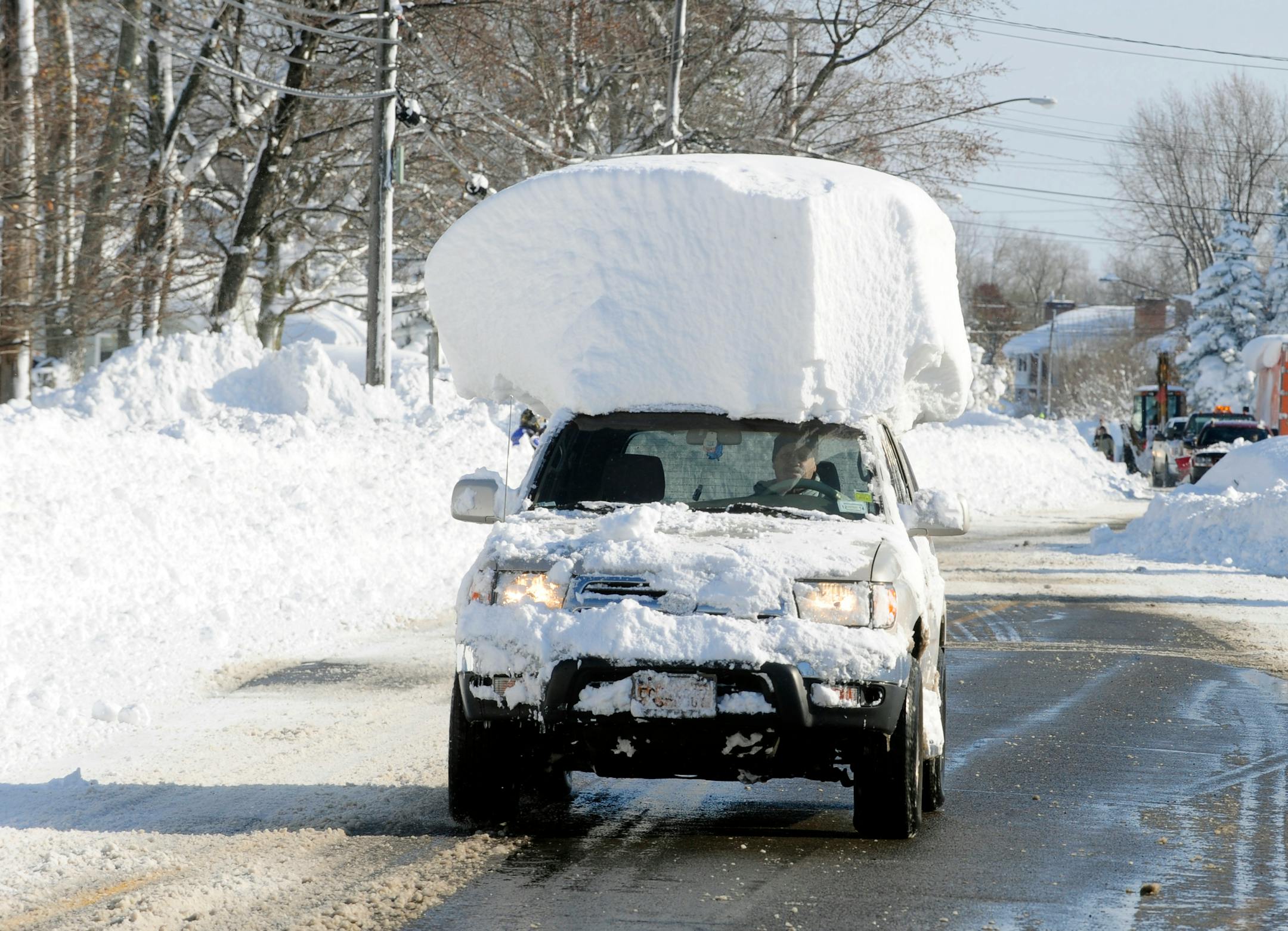 A vehicle, with a large chunk of snow on its top, drives along Route 20 after digging out after a massive snow fall in Lancaster, N.Y. Wednesday, Nov. 19, 2014. Another two to three feet of snow is expected in the area. (AP Photo/Gary Wiepert)
