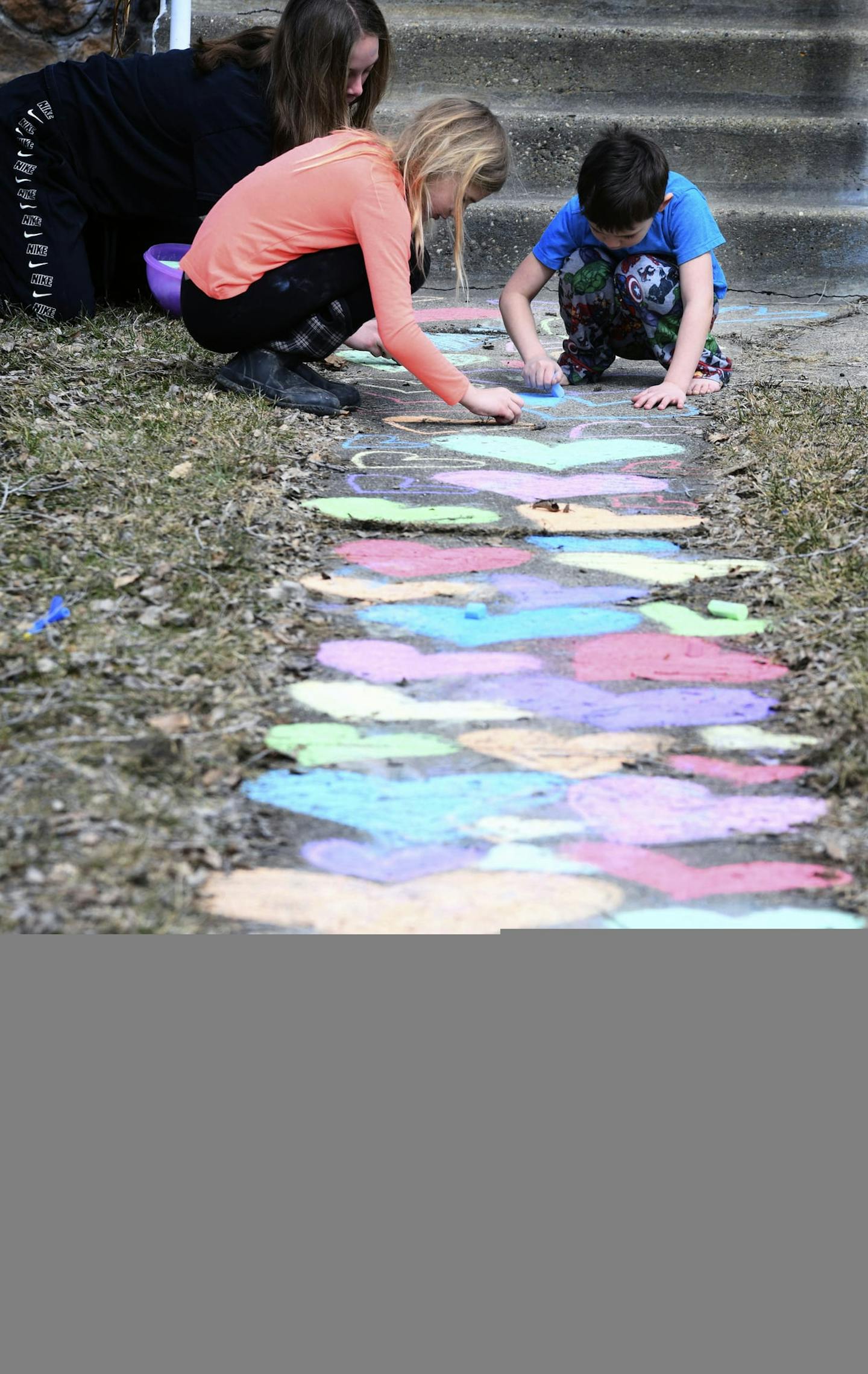 Tanna Crouse, 13, left, Greta Sticha, 8, middle, and her brother Elam, 5, use chalk to color a path of hearts leading to a home's front steps on Tuesday, March 24, 2020 in Bismarck. The hearts are a symbolic gesture of solidarity and a way for people to stay connected while staying at home due to the coronavirus pandemic forcing school closures and social distancing in North Dakota. (Mike McCleary/The Bismarck Tribune via AP) ORG XMIT: NDBIS302