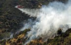 A helicopter makes a water drop on a hillside after a wildfire broke out in the Brentwood area of Los Angeles, Sunday, May 28, 2017. A dark plume of s