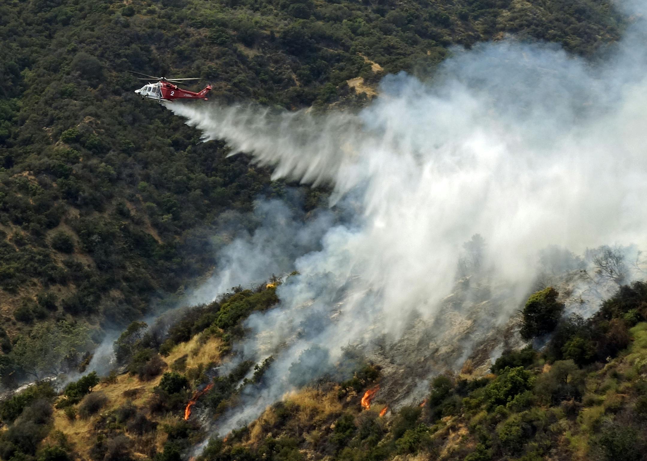A helicopter makes a water drop on a hillside after a wildfire broke out in the Brentwood area of Los Angeles, Sunday, May 28, 2017. A dark plume of smoke was visible for miles as the fire consumed moderate to thick brush near Mandeville Canyon Road, a dead end road that snakes up a deep canyon lined by expensive view homes. A few residents voluntarily left but no homes were damaged. (AP Photo/Brian Melley) ORG XMIT: RPBM703
