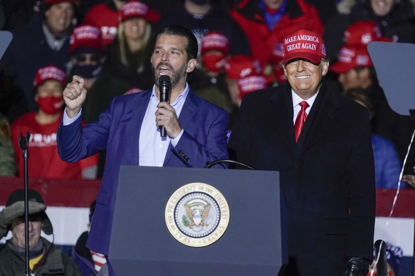 In this Nov. 2, 2020, photo President Donald Trump watches as Donald Trump Jr. speaks at a campaign event at the Kenosha Regional Airport in Kenosha, Wis. A spokesman says President Donald Trump's eldest son, Donald Trump Jr., has been infected with the coronavirus. The spokesman says the younger Trump learned his diagnosis earlier this week, has no symptoms and has been quarantining.