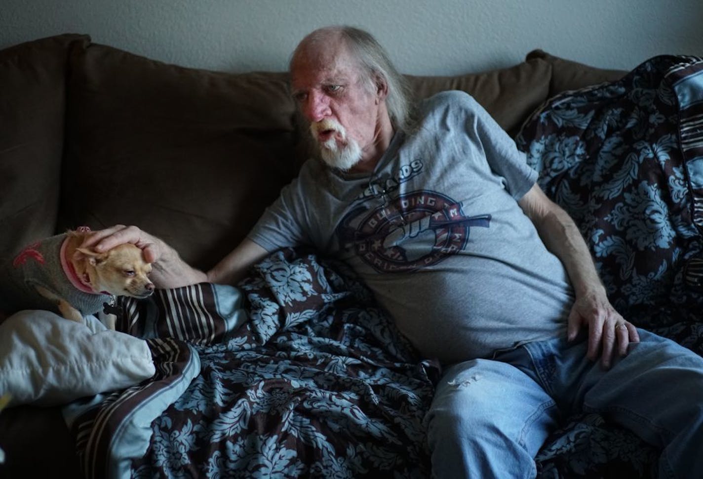 Jerry Larson waits for his granddaughter Mia,9 to come home from school as he rests on the couch with a chihuahua he calls Taco. He wished he could go out to a nearby playground but the back pain makes it too difficult with the reduced opioid prescription.