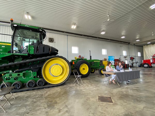 Illinois U.S. Rep. Cheri Bustos and Minnesota U.S. Rep. Angie Craig, both Democrats, sit at a table near a John Deere tractor in a farm shed east of N