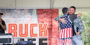 Mike Waldron hugs a man in a stars and stripes outfit while standing on a stage.