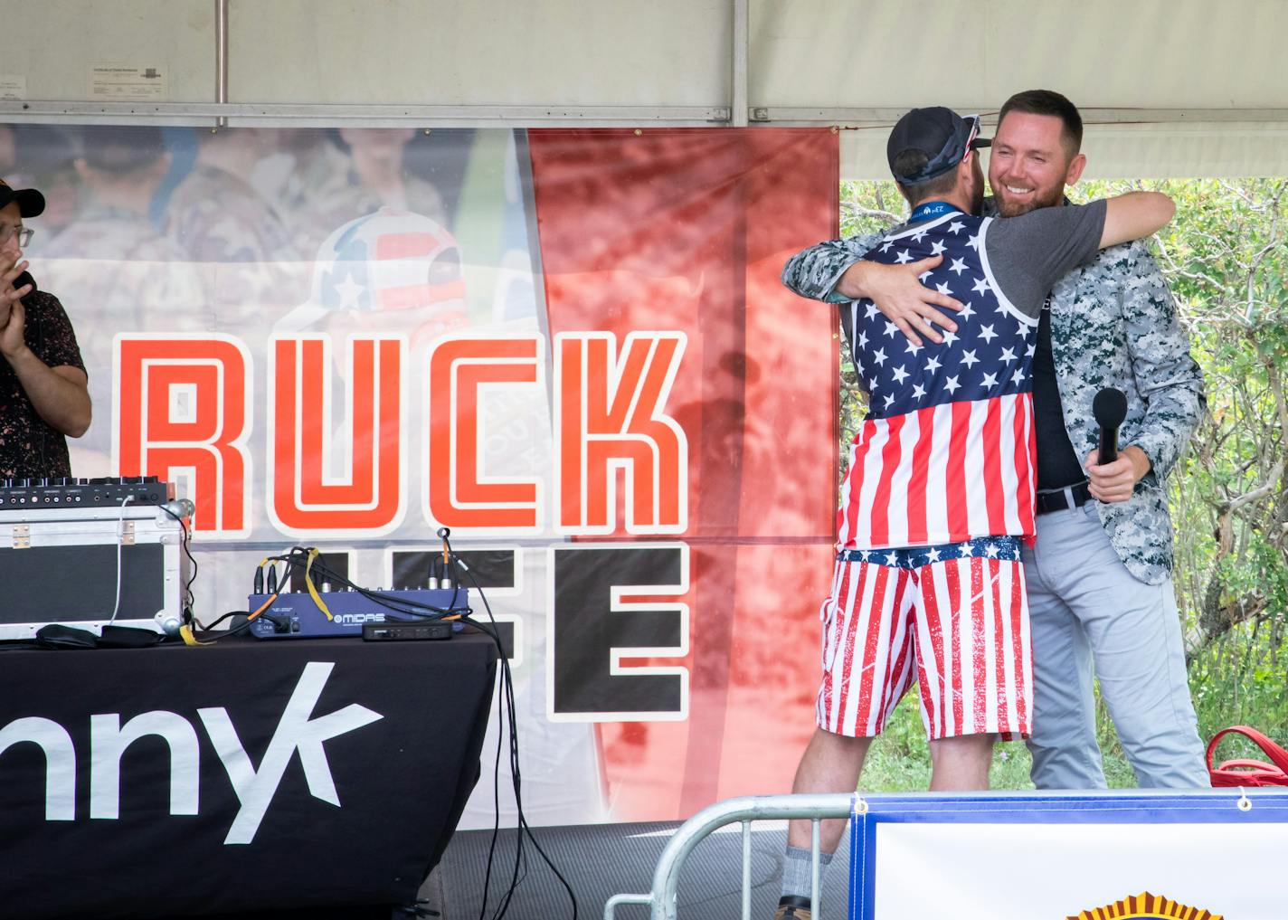 Mike Waldron hugs a man in a stars and stripes outfit while standing on a stage.