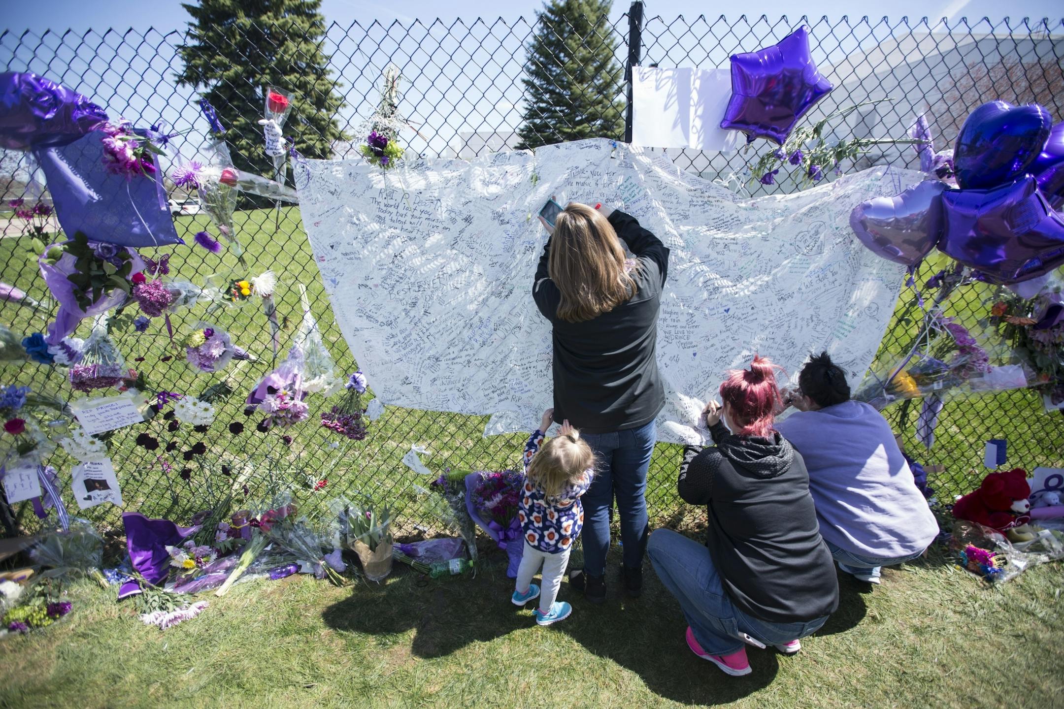 People signed a sheet with messages at the memorial for Prince set up on the fence outside his home at Paisley Park on Friday, April 22, 2016, in Chanhassen, Minn..