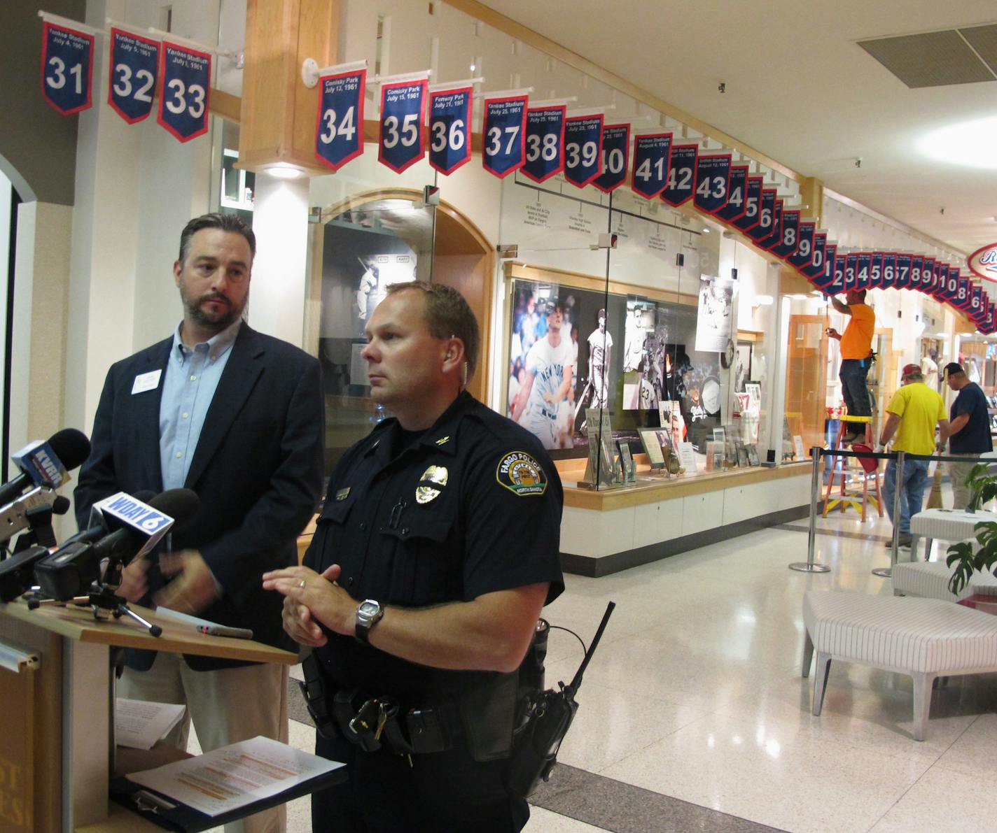 West Acres Mall property manager Chris Heaton, left, and Fargo Deputy Police Chief Joe Anderson talk in front of the Roger Maris Museum in Fargo, N.D., on Tuesday, July 26, 2016, while workers repair a display where an ornate belt was stolen from the mall early Tuesday. Maris, who grew up in Fargo, won the Hickok Belt in 1961 when he hit 61 home runs, a record at the time. The award has gone to the top professional athletes in the country. (AP Photo/Dave Kolpack)