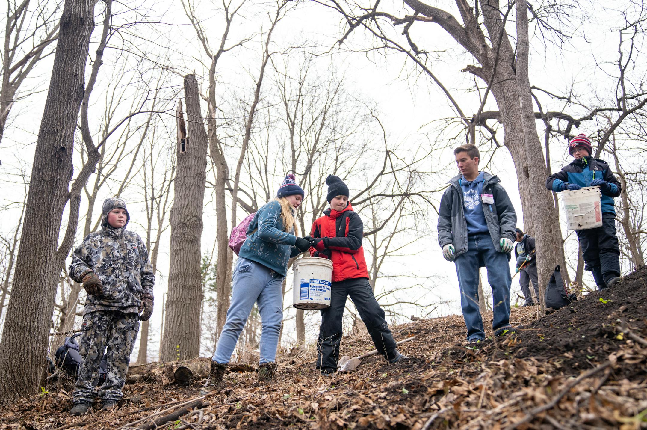 Members of scout troop 695 from Eden Prairie form a chain to hand buckets of dirt up a hill as part of a tree planting event Saturday, April 22, 2023, on a Nature Hiking Trail leading to the Minnesota River in Bloomington.