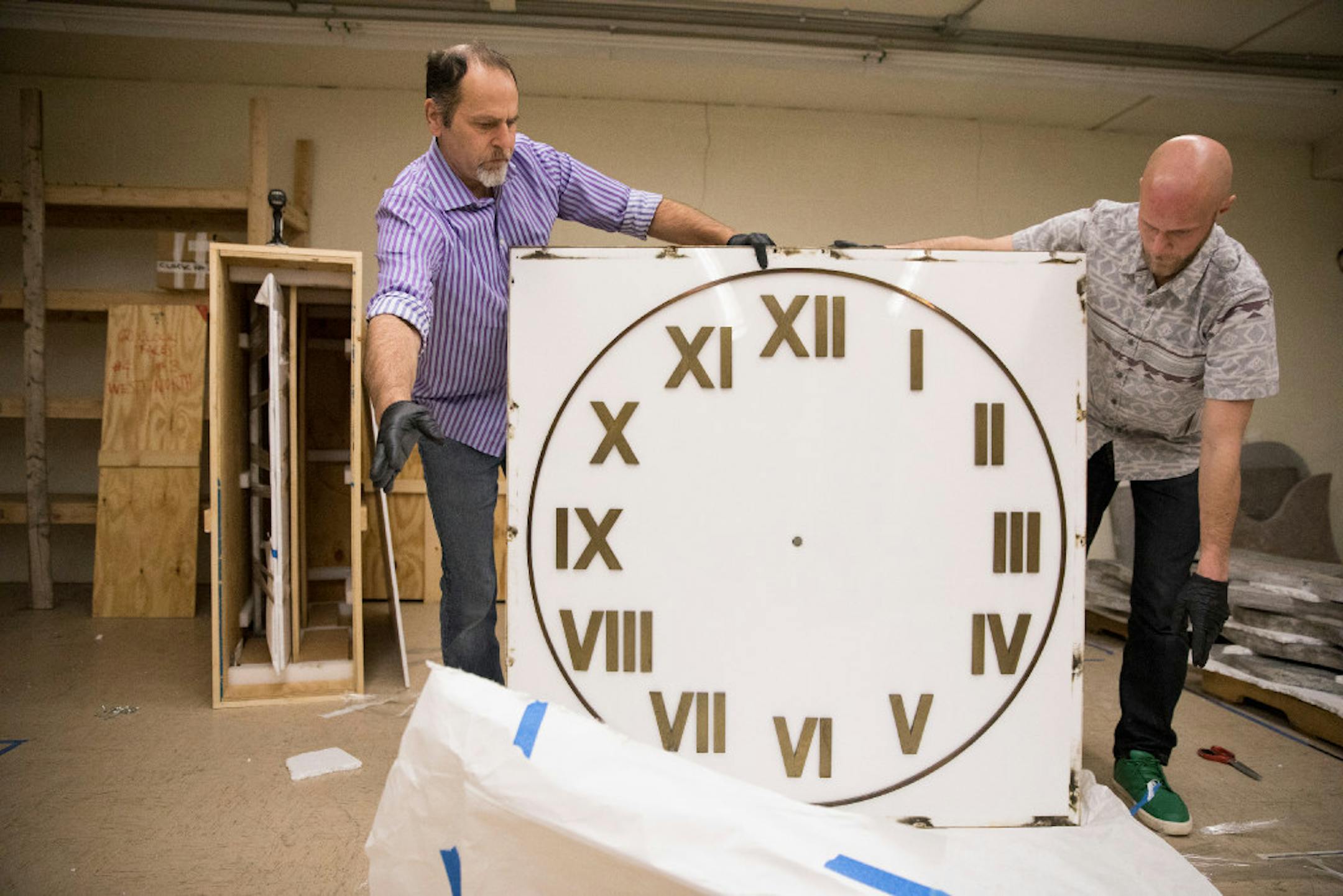 Art preparators Joel Pieper, left, and Nick Sparby of Joel Pieper Fine Arts unwrap one of the faces of the Sculpture Clock. Parts of the 16-foot-clock are in storage in the basement of the IDS Building