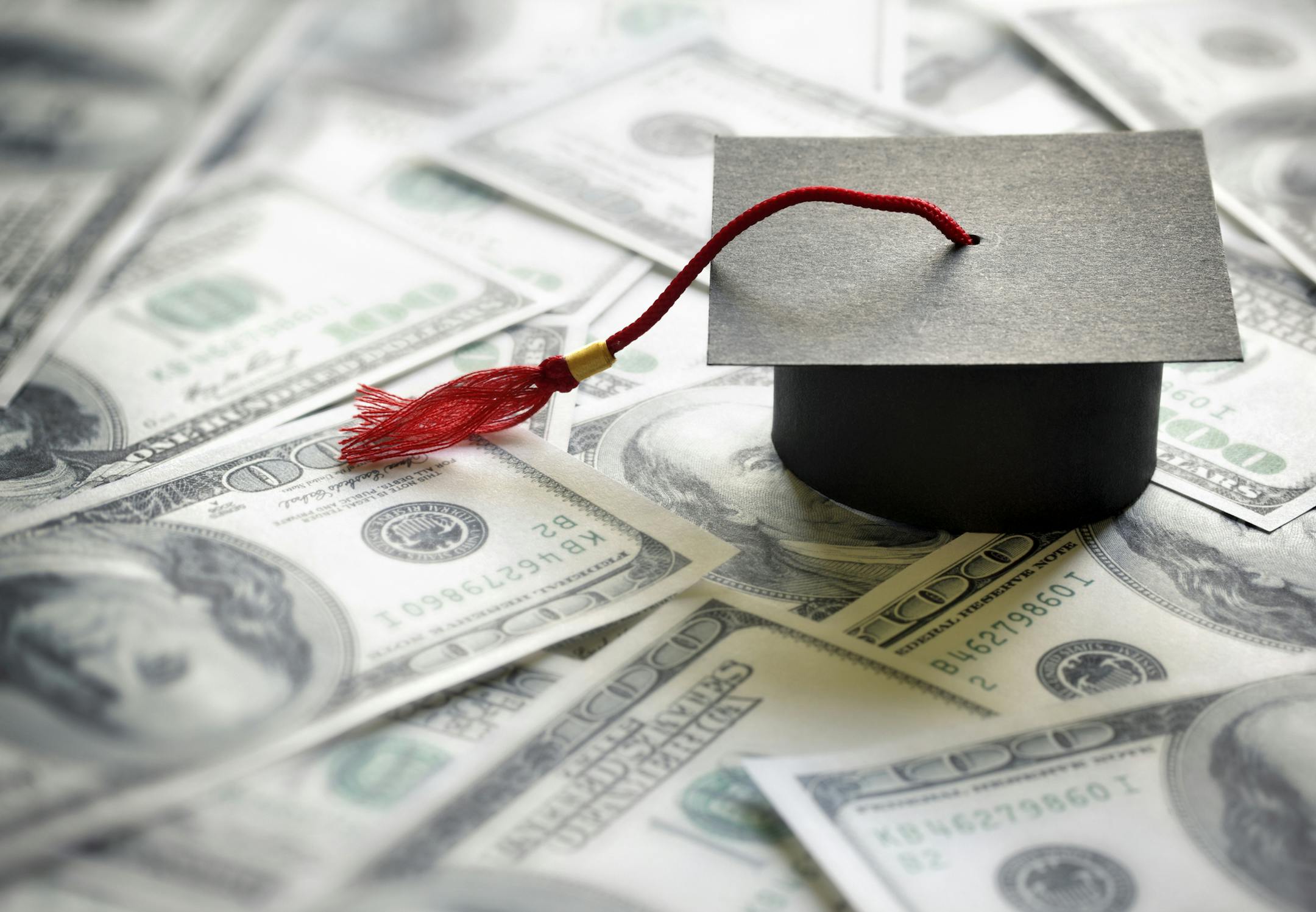 Graduation mortar board cap on one hundred dollar bills concept for the cost of a college and university education. istock photo
