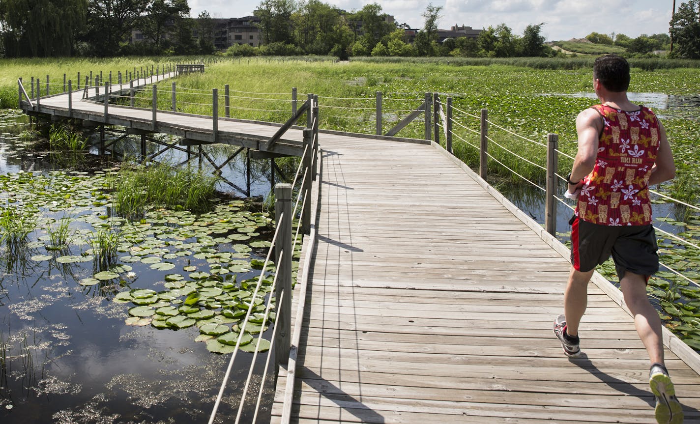 A jogger runs on the elevated walkway that juts through Lake Camelot in Plymouth on Monday, July 27, 2015. ] LEILA NAVIDI leila.navidi@startribune.com / BACKGROUND INFORMATION: Lake Camelot used to be called Mud Lake.