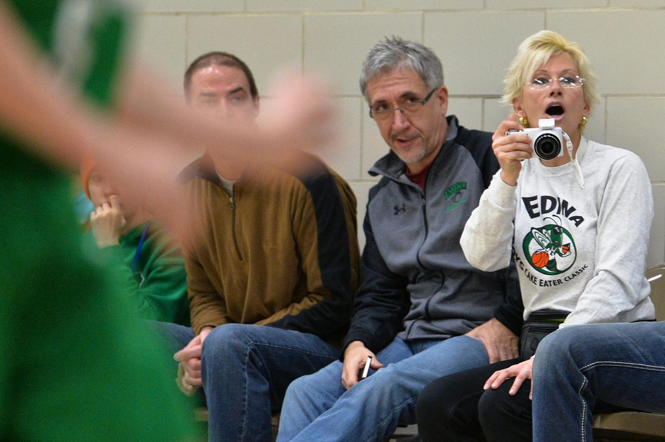 Edina 4A boys' traveling basketball team parent, Giovanna Ingram, uses a camera to record video of her son, Vinnie's game performance. Ingram's husband, Terry's landscape business, Lawn-N-Order, sponsors the team, placing the company's logo on the boys' warm-up shirts.