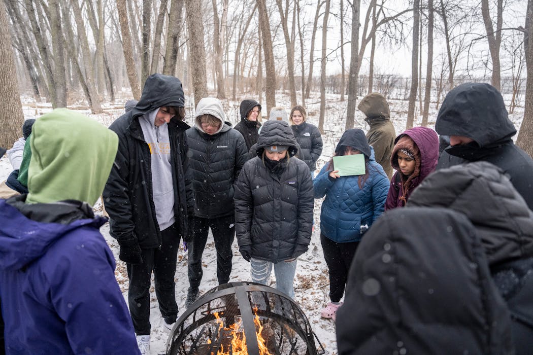 Students in Julia Battern’s Ecology class stay warm huddled around a fire in the woods behind Mankato East High School on Thursday, Jan. 18.