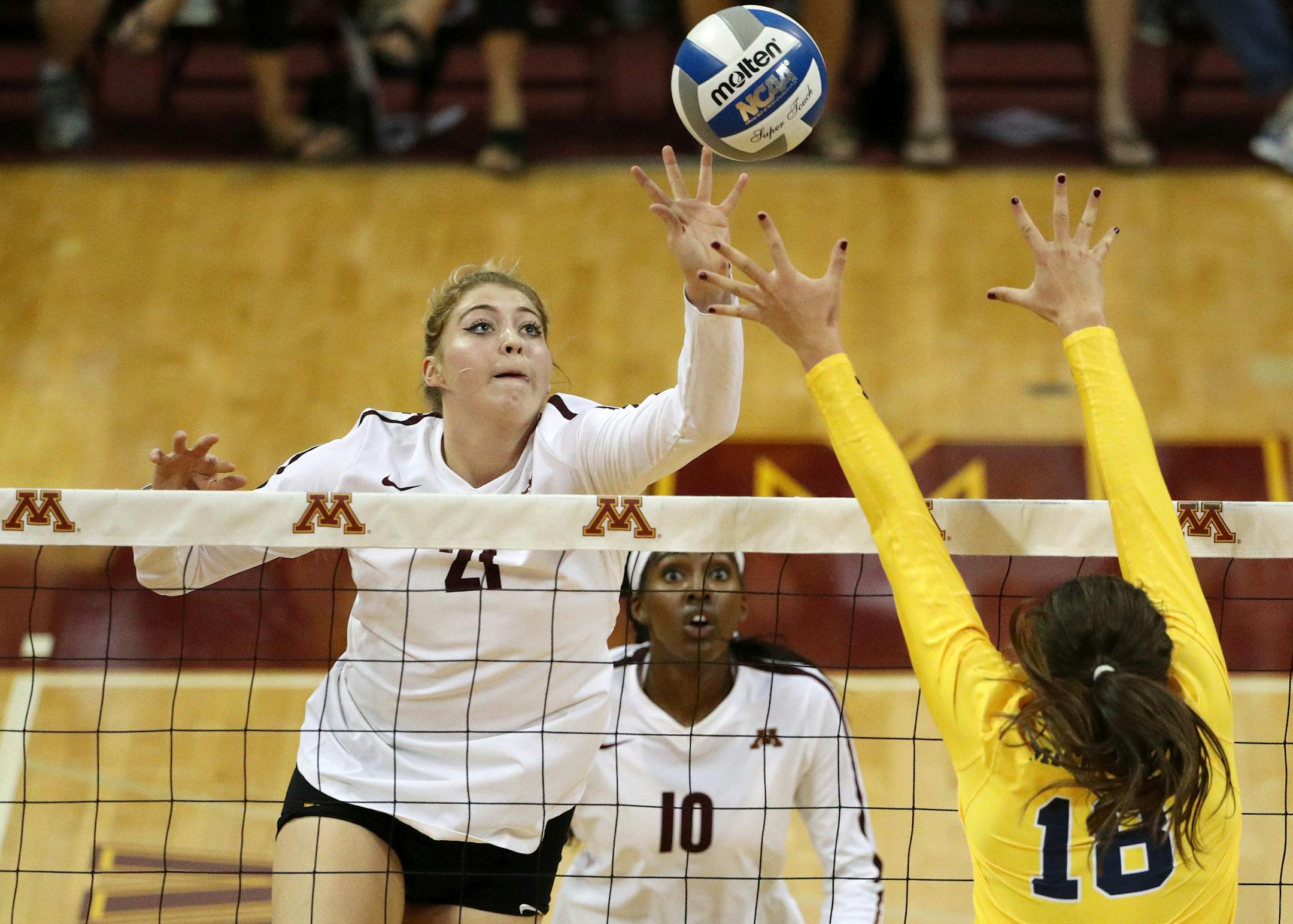 Gophers middle blocker Regan Pittman (21) sent the ball over the net as Michigan outside hitter Carly Skjodt (18) leapt to defend in the first set Friday night.
