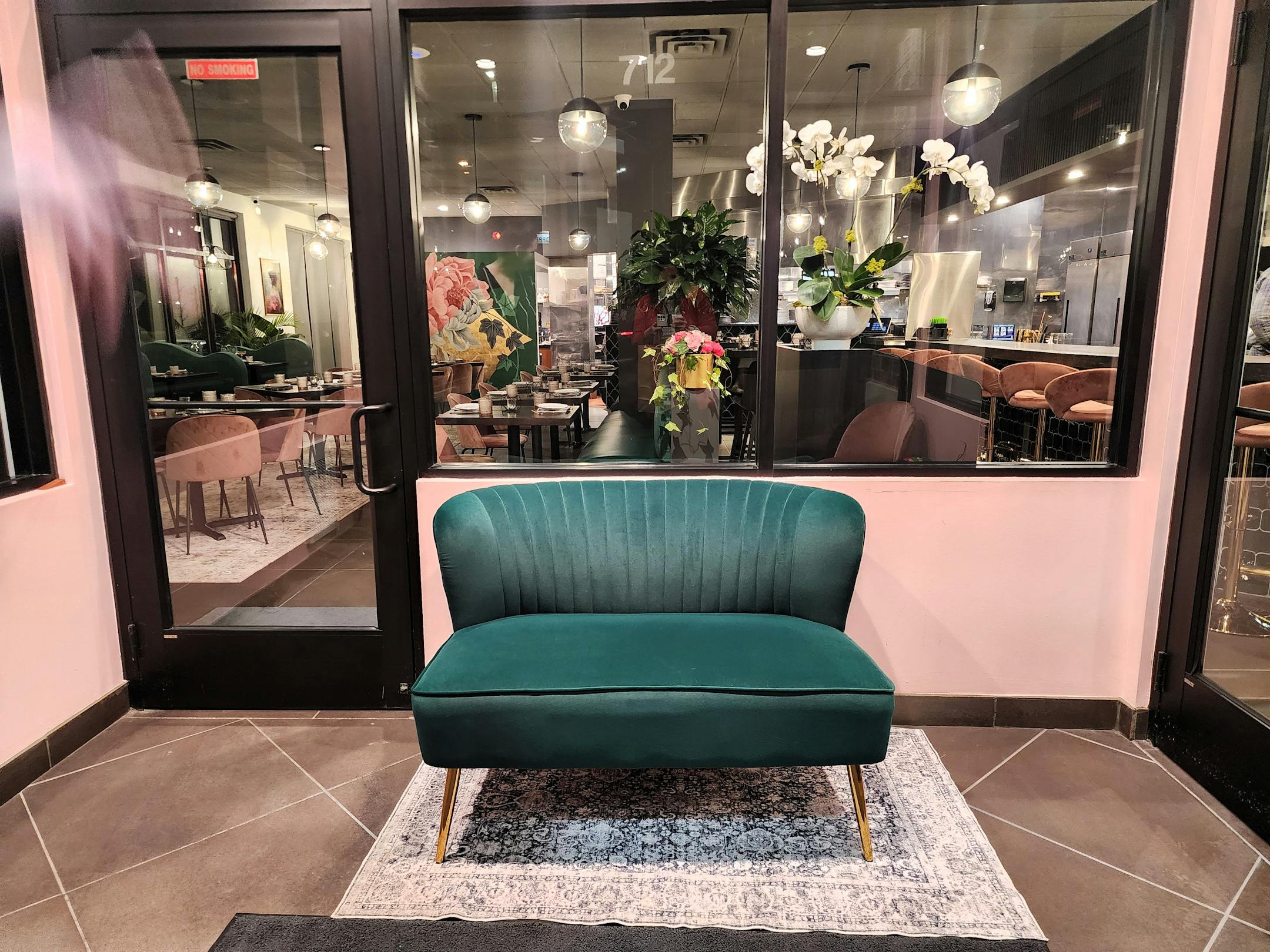 A green couch in front of a pink wall and underneath windows into a brightly lit restaurant